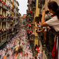 Balconies full of spectators on Calle Estafeta (Estafeta Street) watch the Pamplona bull run. Bulls and runners in the street below are blurry, capturing their speed. 
